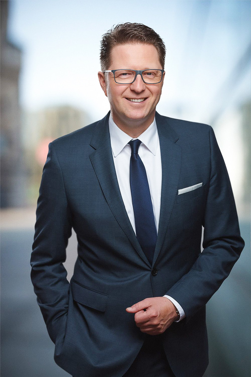 Businessportrait eines Geschäftsführers im Anzug vor städtischem Hintergrund
